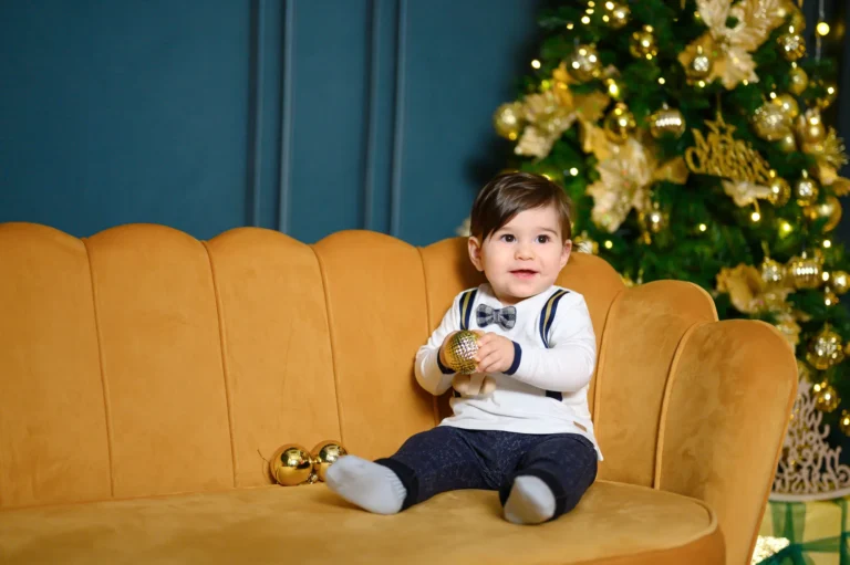 Bimbo seduto su un divano giallo con luci di Natale, foto di Natale in studio a Venaria Reale