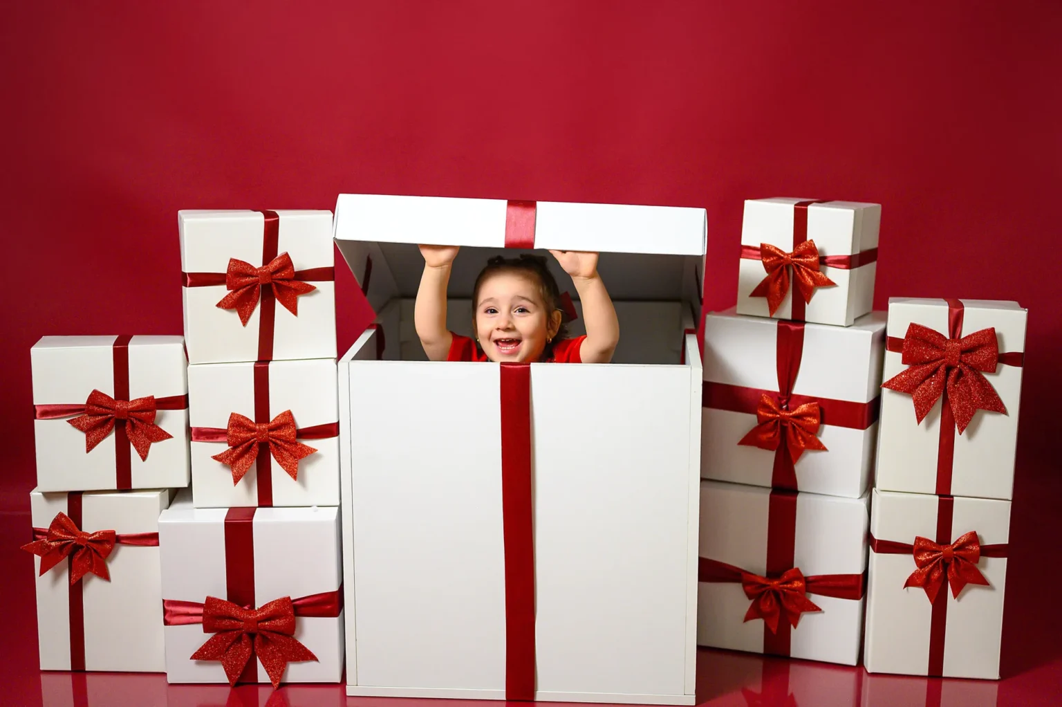Bambina che sbuca da un regalo bianco con fiocco rosso, foto di Natale in studio