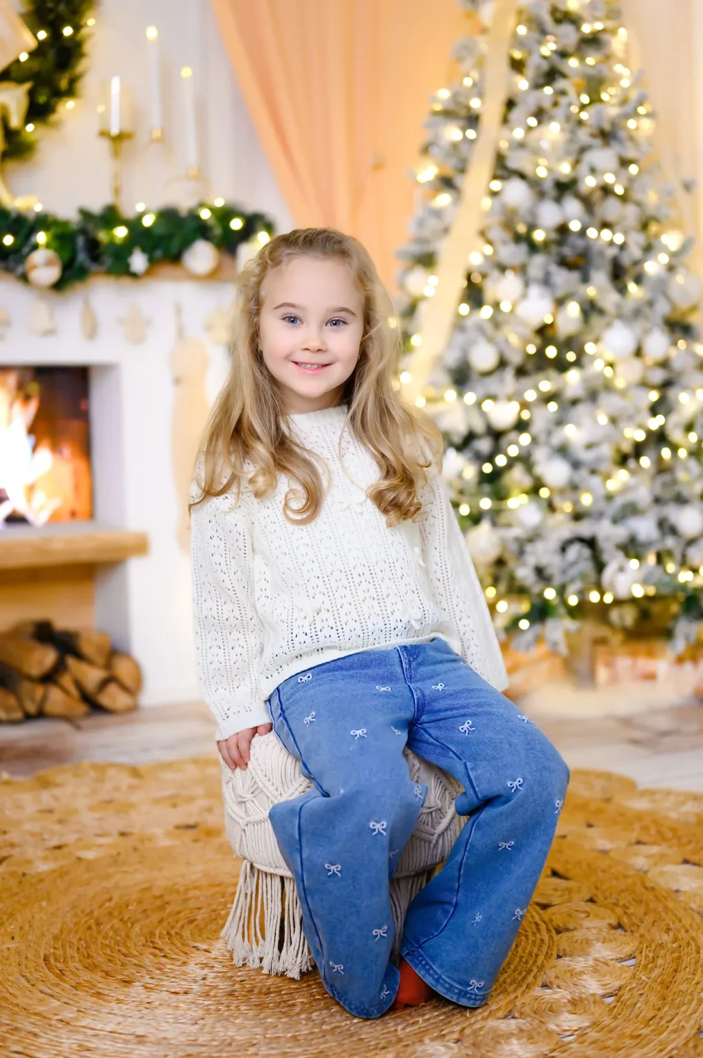 Bambina in maglione bianco davanti all’albero di Natale illuminato, ritratto in studio