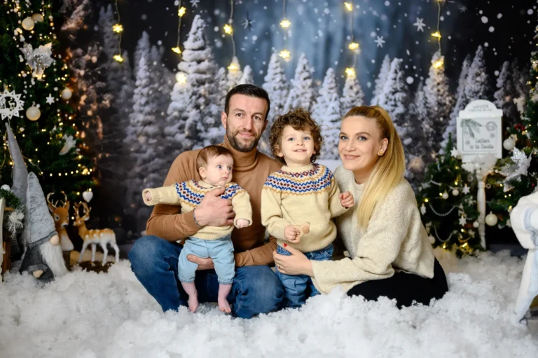 Famiglia con due bambini piccoli sulla neve finta tra abeti innevati, foto di Natale in studio a Venaria Reale