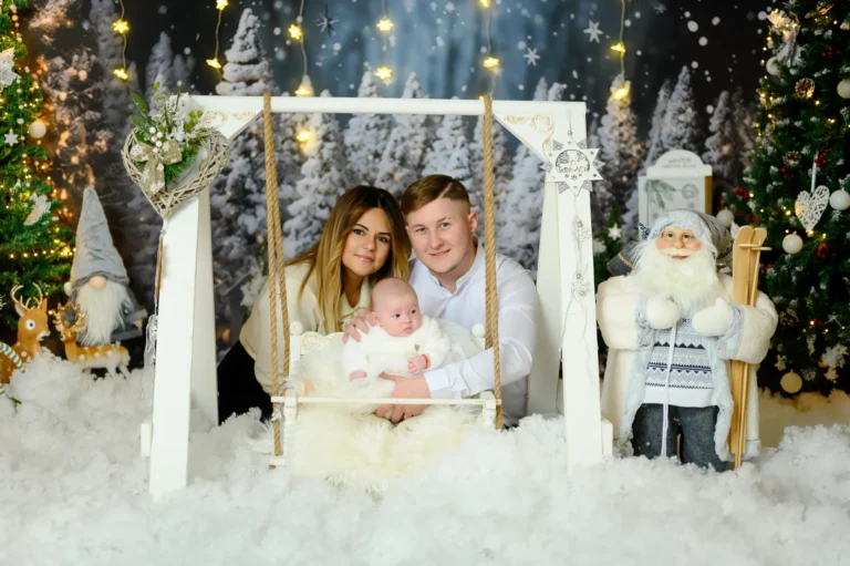 Mamma e papà con neonata sull’altalena bianca accanto a Babbo Natale, foto di famiglia a Natale
