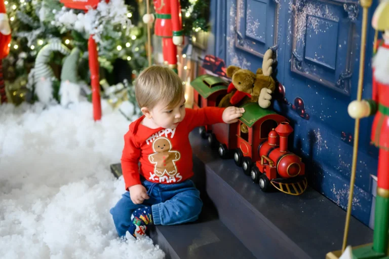 Bambino con trenino giocattolo tra neve finta e luci, fotografia natalizia in studio a Torino