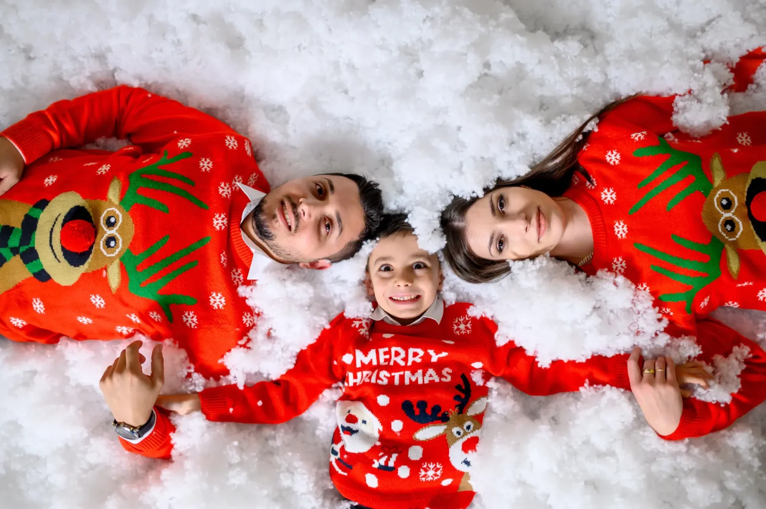 Famiglia in maglioni natalizi sdraiata sulla neve finta, foto di Natale in studio a Venaria Reale